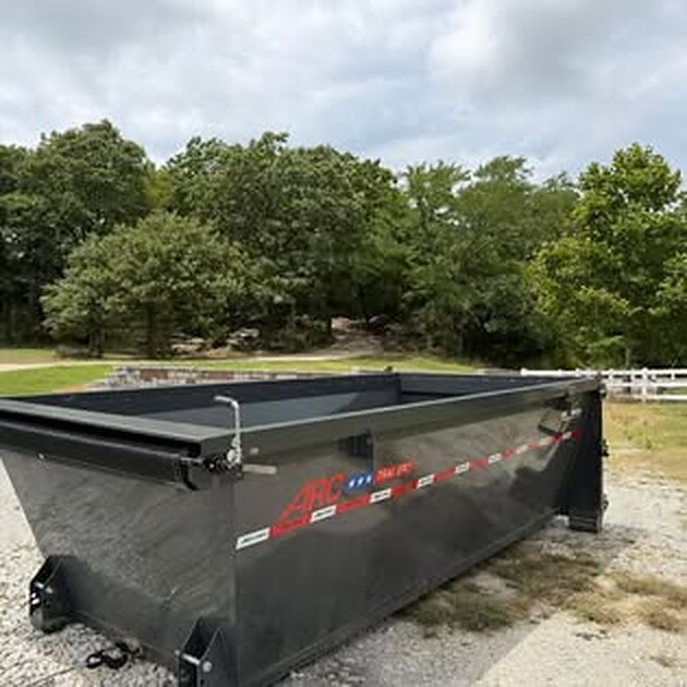 Black SCORO roll-off bin on a gravel driveway with trees behind it