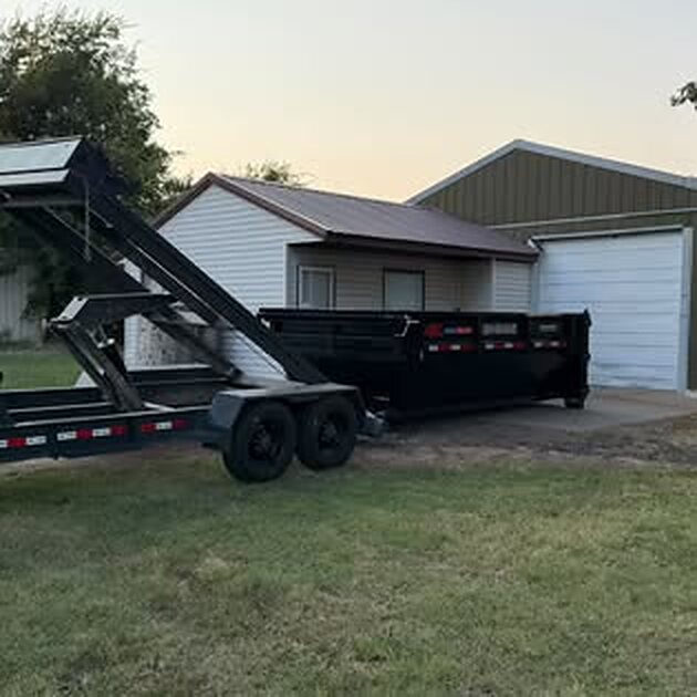 SCORO roll-off bin delivered on a concrete pad beside a metal shop at dusk