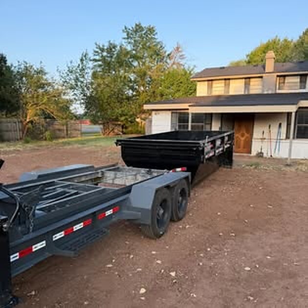 SCORO delivery trailer pulling away from a black roll-off bin placed in front of a home