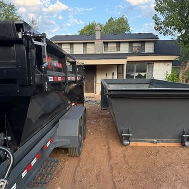 SCORO roll-off bin set on red dirt in front of a two-story house, with the delivery trailer alongside